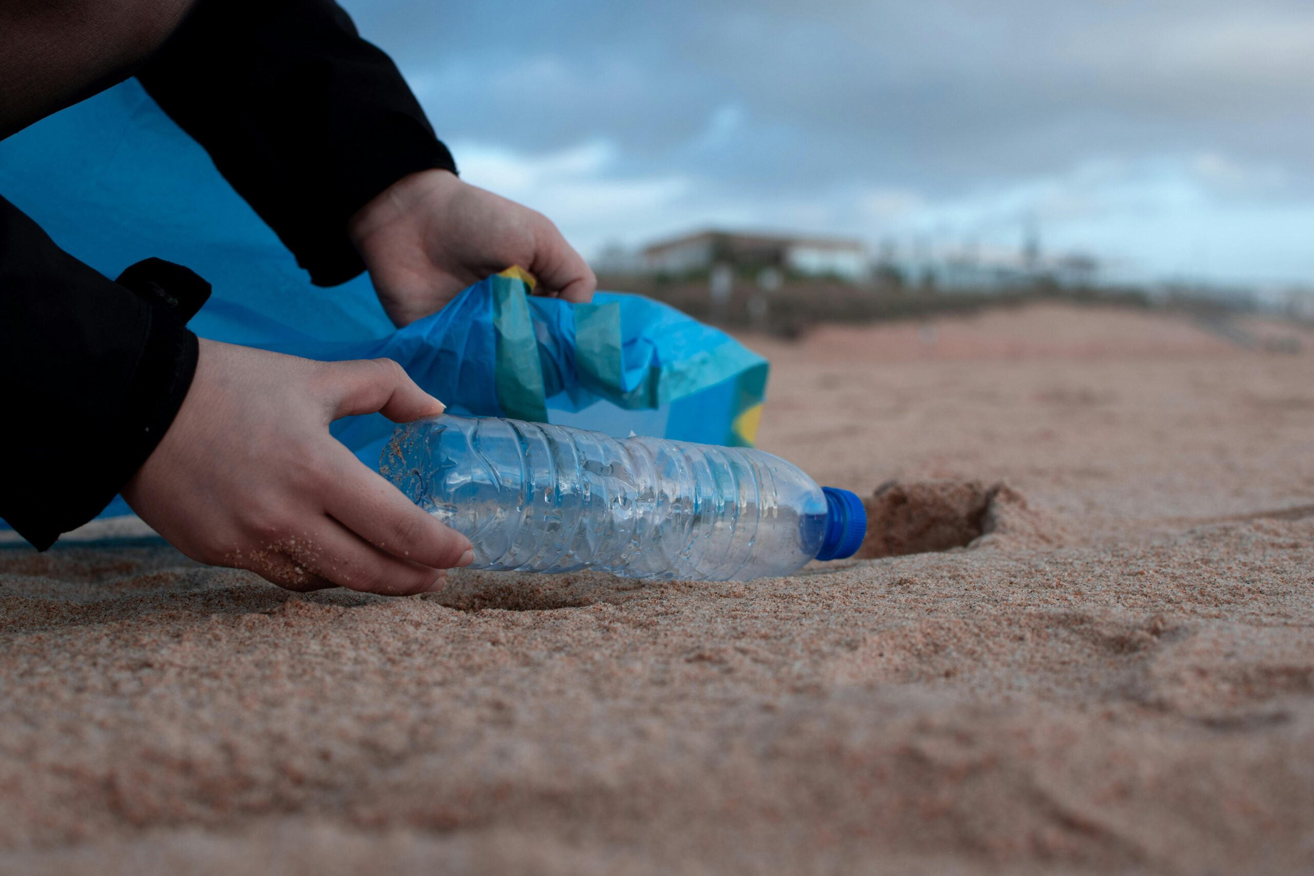 person disposing of clear plastic bottle littering beach